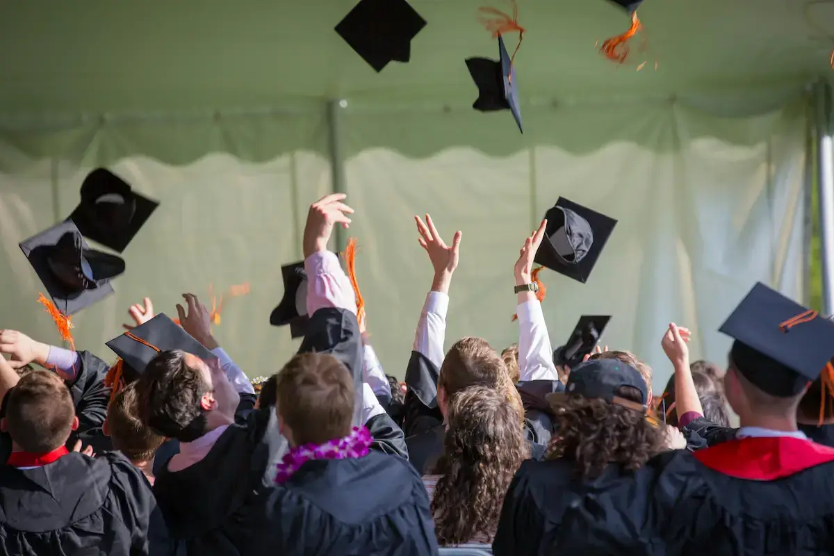 Group of graduates in black gowns tossing their caps in the air during a graduation ceremony.