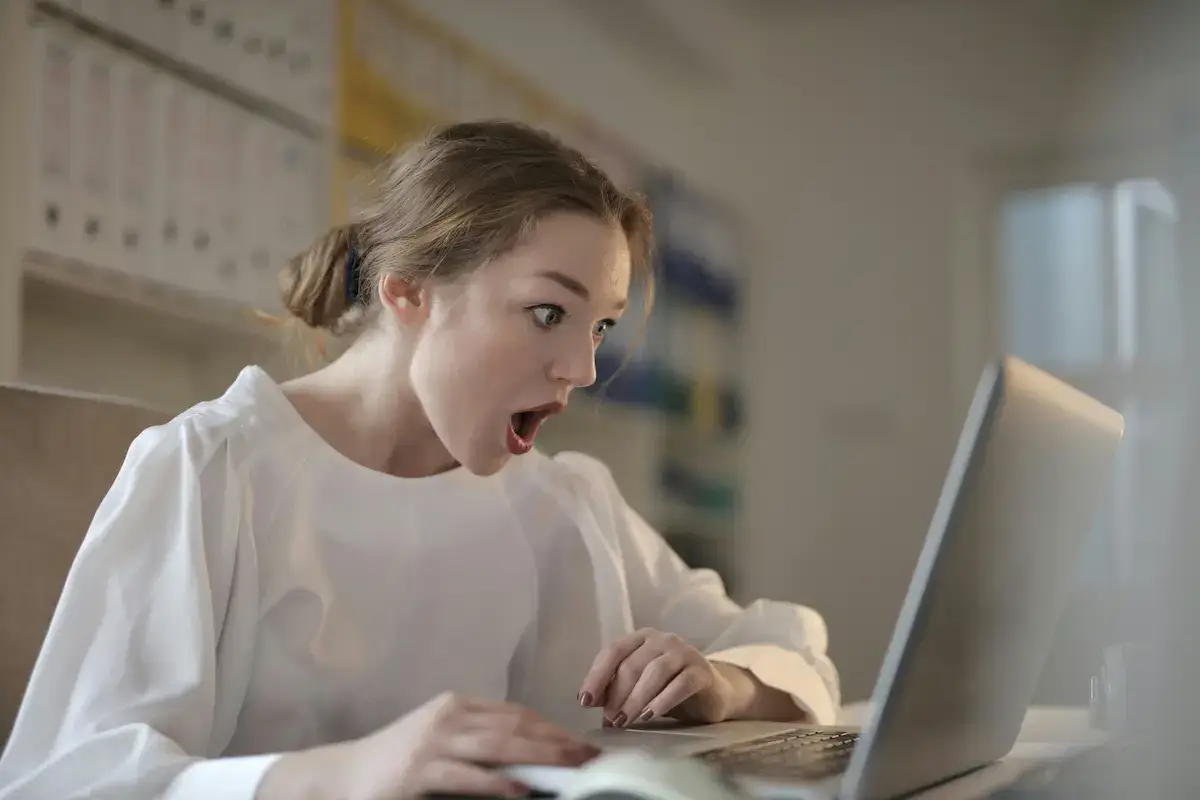 Surprised young woman looking at laptop screen with an open mouth in a softly lit room.